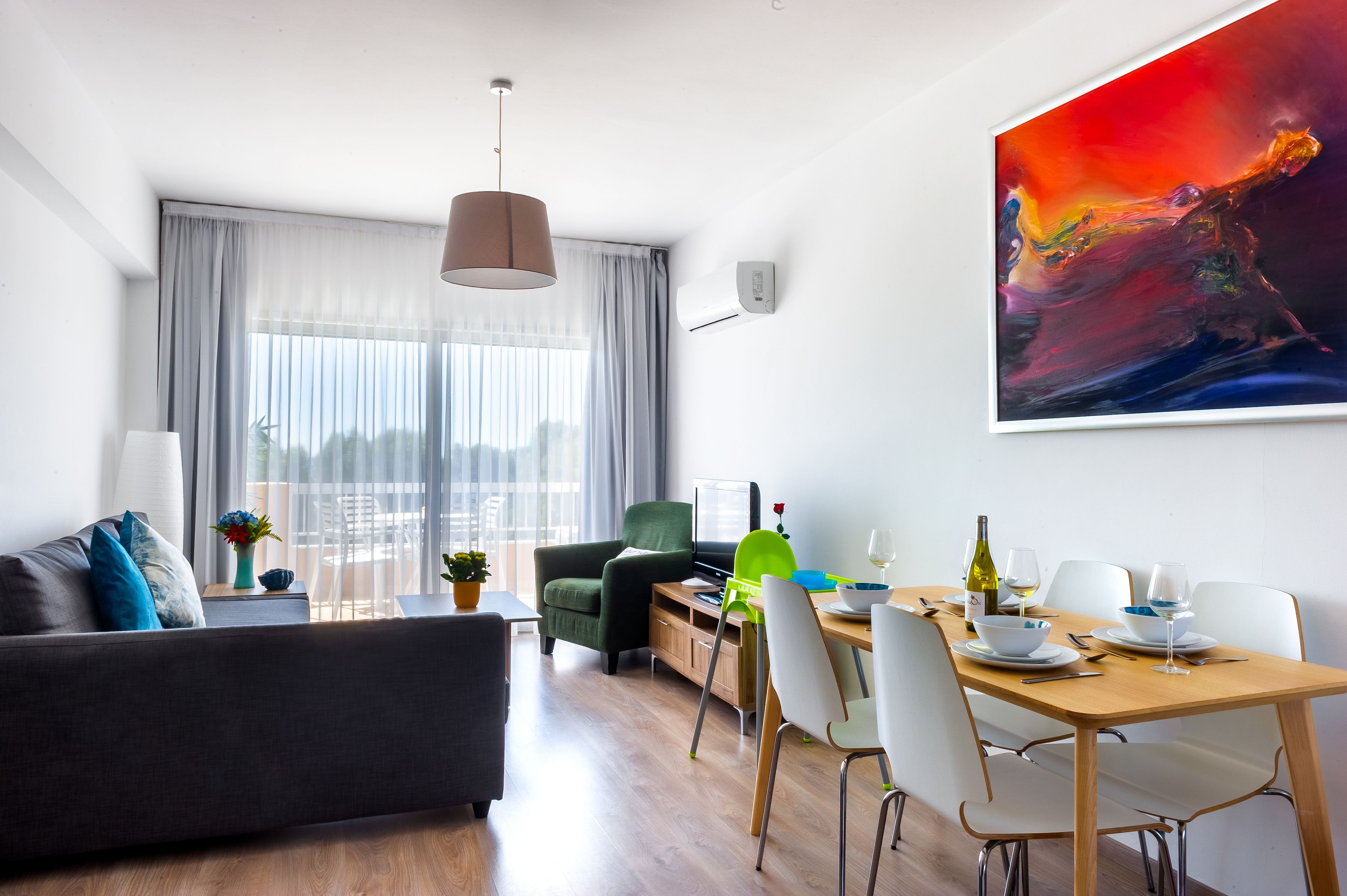 A modern living room with a sofa, dining table, chairs, and a painting.
