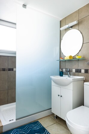 Un bagno moderno con cabina doccia in vetro, un lavandino bianco e un dispenser di sapone blu, e un water.