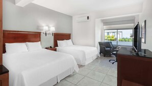 A hotel room with two beds, a desk, a chair, a TV, and a window with a view of greenery. - Days Inn by Wyndham Piedras Negras (Piedras Negras)