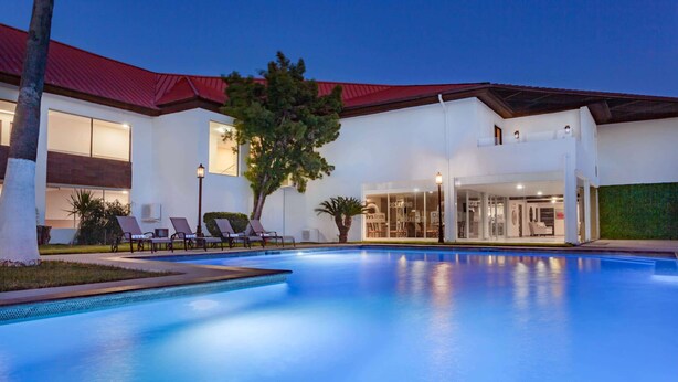 A modern building with a swimming pool, lounge chairs, and a red roof. - Days Inn by Wyndham Piedras Negras (Piedras Negras)
