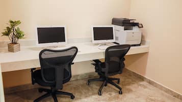 Un espacio de trabajo con dos escritorios, dos sillas, dos monitores, una impresora y una pequeña planta en maceta.