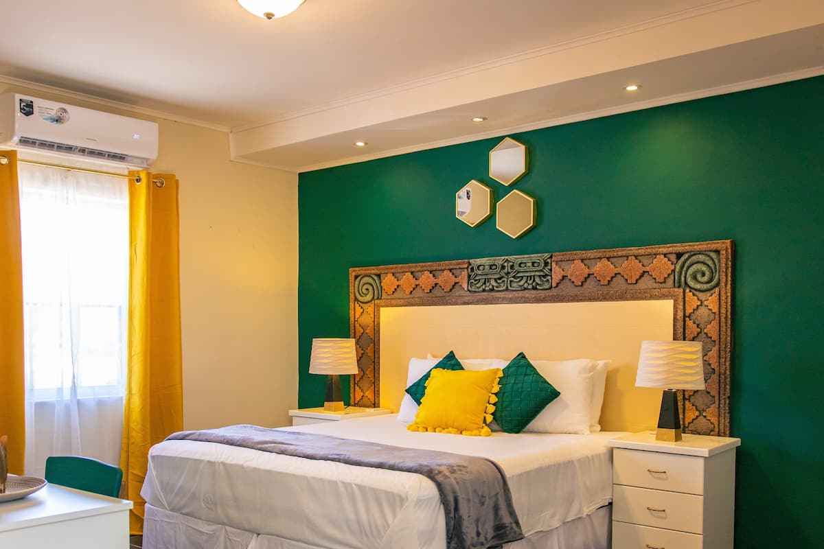 A hotel room with a bed, bedside tables, a nightstand, a mirror, and a window with curtains.