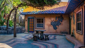 A rustic building with a tiled roof, a stone wall, and a wooden table with benches.