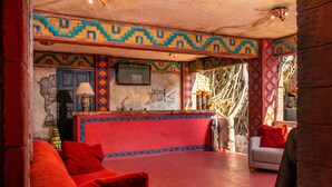 A room with a red sofa, a small table, and a bar area with a TV.
