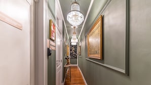 A hallway with a chandelier, framed artwork, and a wooden floor.