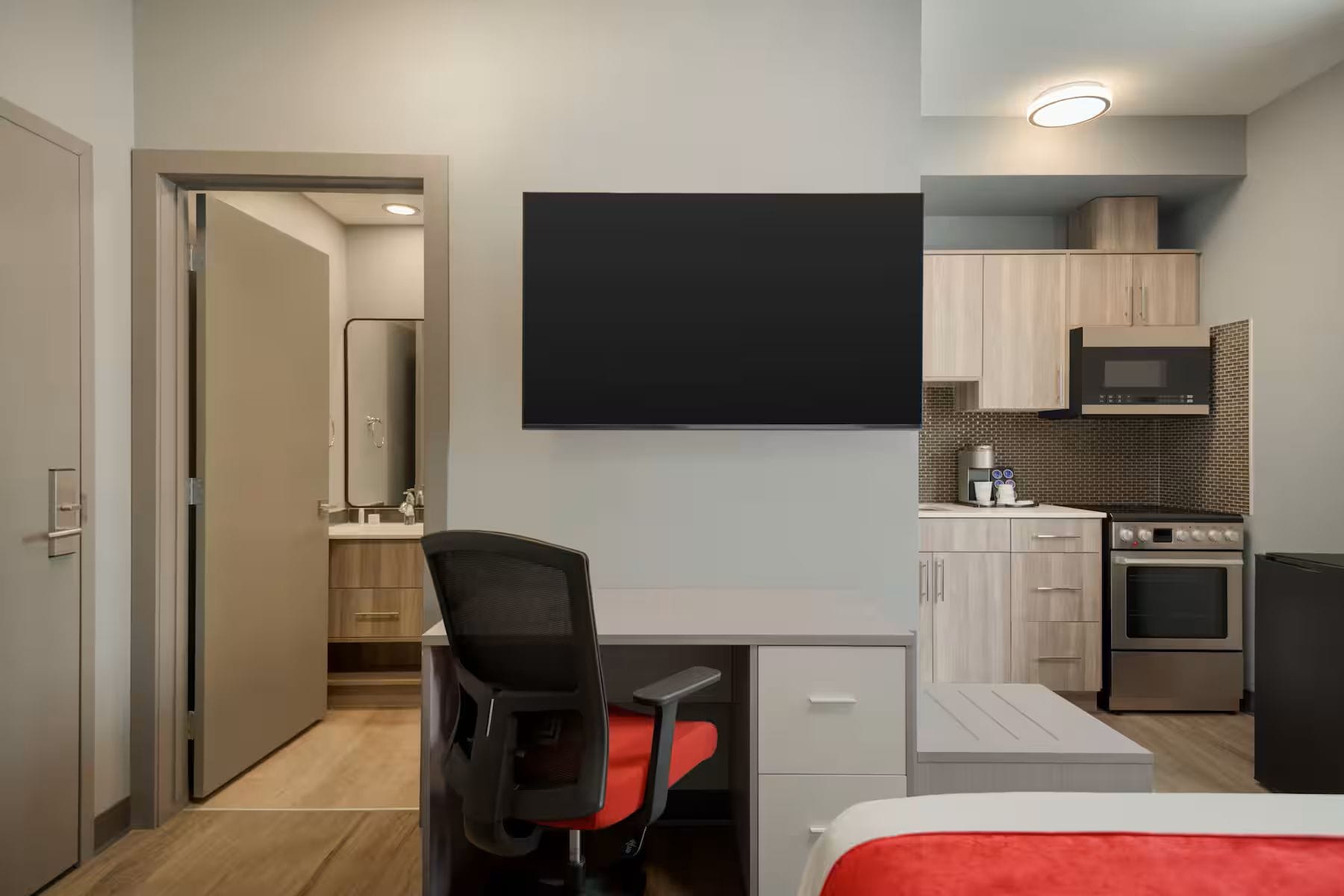 Una habitación de hotel moderna con escritorio, silla, cama y kitchenette.