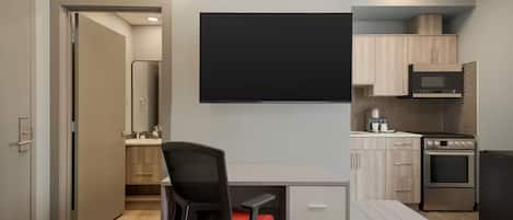Una habitación de hotel moderna con escritorio, silla, cama y kitchenette.