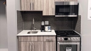 A compact kitchen with light wood cabinets, a stainless steel microwave, a coffee maker, and a stove.