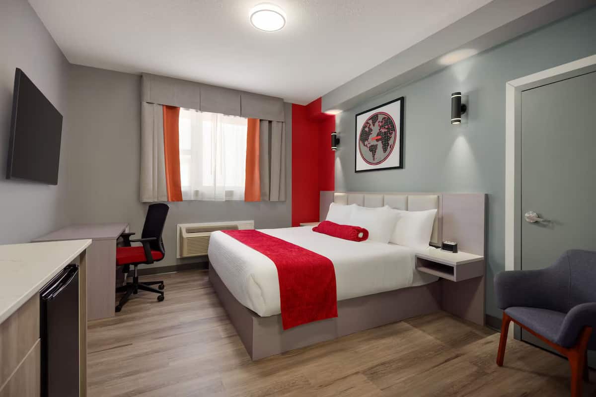Una habitación de hotel moderna con cama, mesita de noche, silla, escritorio y ventana con cortinas.