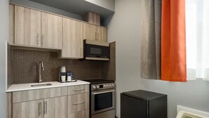 A compact kitchen with light wood cabinets, a black microwave, a coffee maker, and a black refrigerator.