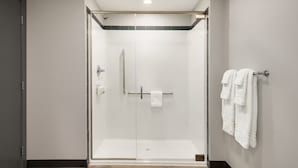 Un espace douche moderne doté d’une porte en verre, d’un porte-serviettes avec des serviettes et d’un panneau de commande de douche bien visible.