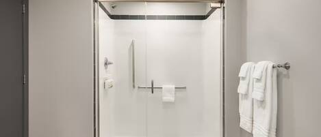 A modern shower area with a glass door, a towel rack with towels, and a visible shower control panel.