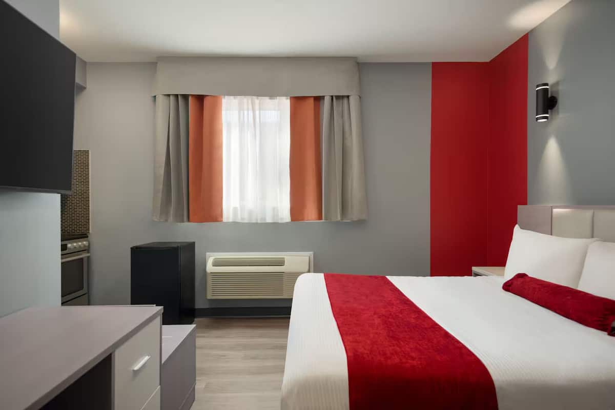 Una habitación de hotel con cama, escritorio, calefacción y ventana con cortinas.