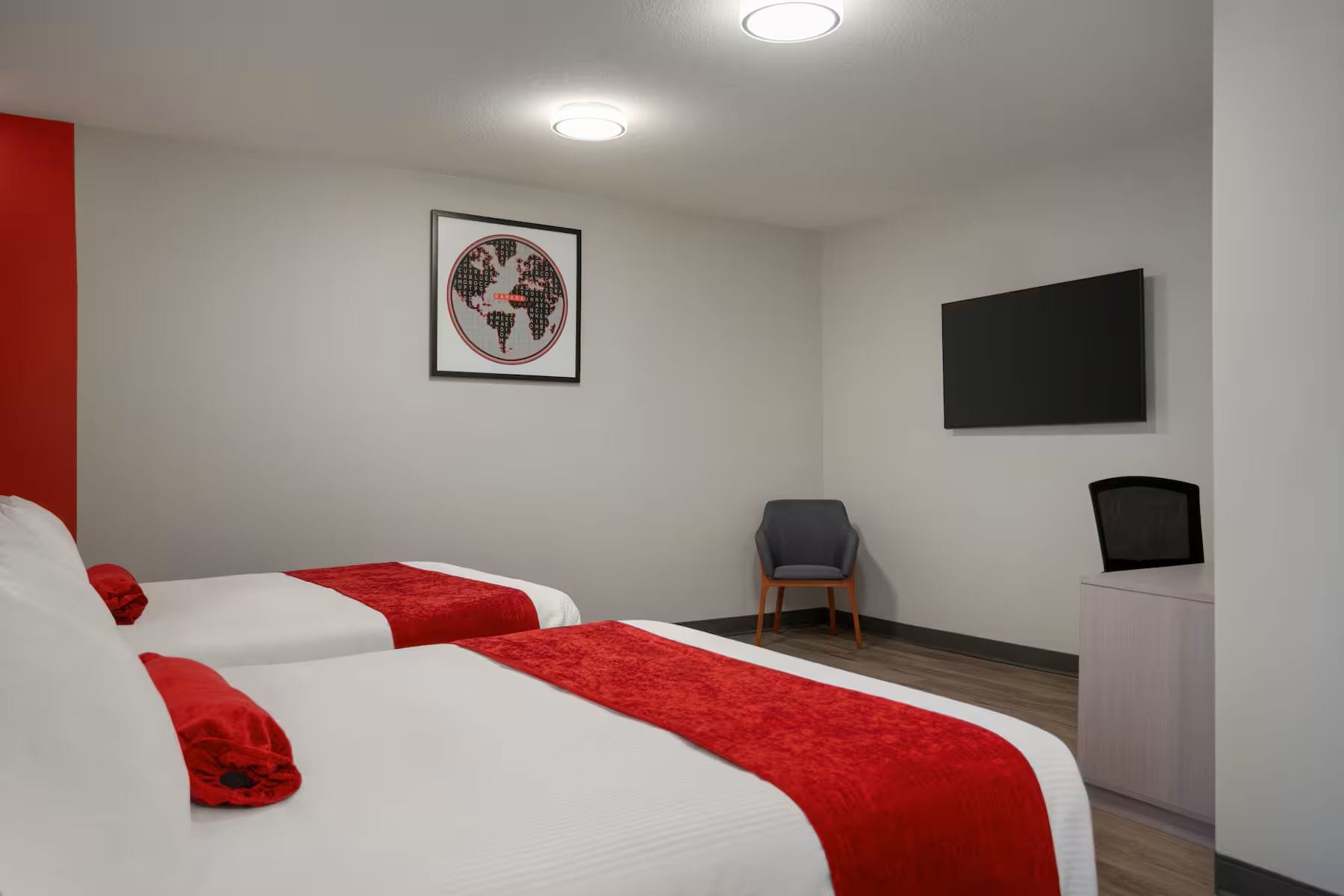 Habitación de hotel con dos camas, una silla, un televisor de pantalla plana y un mapa mundial enmarcado en la pared.