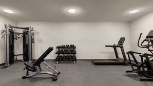 Une salle de sport équipée d’un support à squats, d’un banc de développé couché, d’haltères, d’un tapis de course et d’un vélo d’appartement.