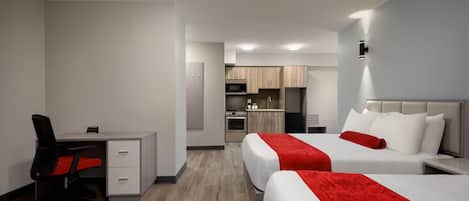 A hotel room with two beds, a desk, and a kitchenette.