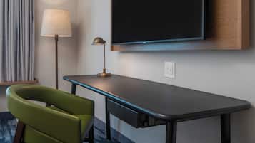 Una habitación de hotel moderna con una televisión de pantalla plana en la pared, un escritorio con lámpara y una silla verde.