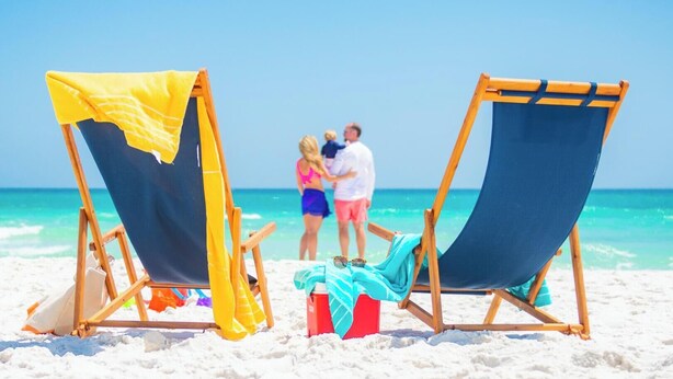 Two beach chairs with towels, a cooler, and a beach umbrella on a sandy beach with a clear blue sky. - Fairfield by Marriott Inn & Suites Pensacola Pine Forest (Pensacola)