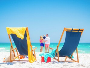 Two beach chairs with towels, a cooler, and a beach umbrella on a sandy beach with a clear blue sky. - Fairfield by Marriott Inn & Suites Pensacola Pine Forest (Pensacola)