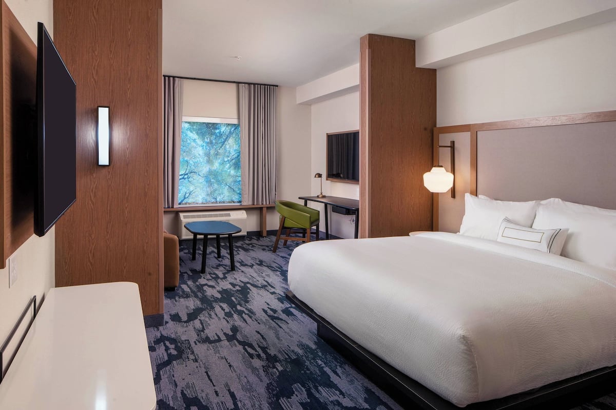 A hotel room with a large bed, a desk, a chair, a television, and a window with curtains.
