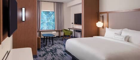 Une chambre d’hôtel avec un grand lit, un bureau, une chaise, une télévision et une fenêtre avec des rideaux.
