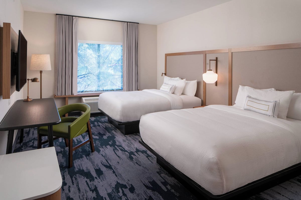 A hotel room with two beds, a desk, a chair, a TV, and a window with curtains.