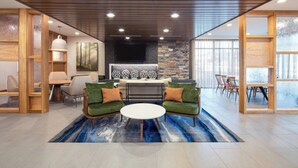 A modern living room with a fireplace, green sofas, and a dining area with wooden furniture. - Fairfield by Marriott Inn & Suites Pensacola Pine Forest (Pensacola)