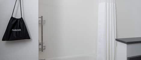 A modern bathroom with a bathtub, a towel rack, and a black bag hanging on the wall.
