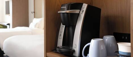 A Keurig coffee maker with two mugs on a tray, a power outlet, and a small basket with a cup.
