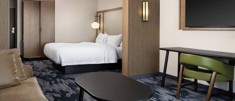 A hotel room with a bed, a desk, a green chair, a sofa, and a wall-mounted TV.