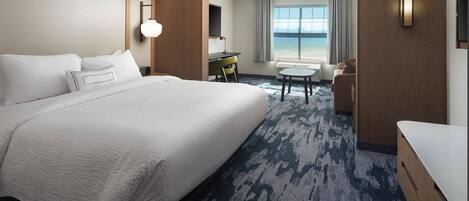 A hotel room with a large bed, a desk, a chair, and a view of the ocean.