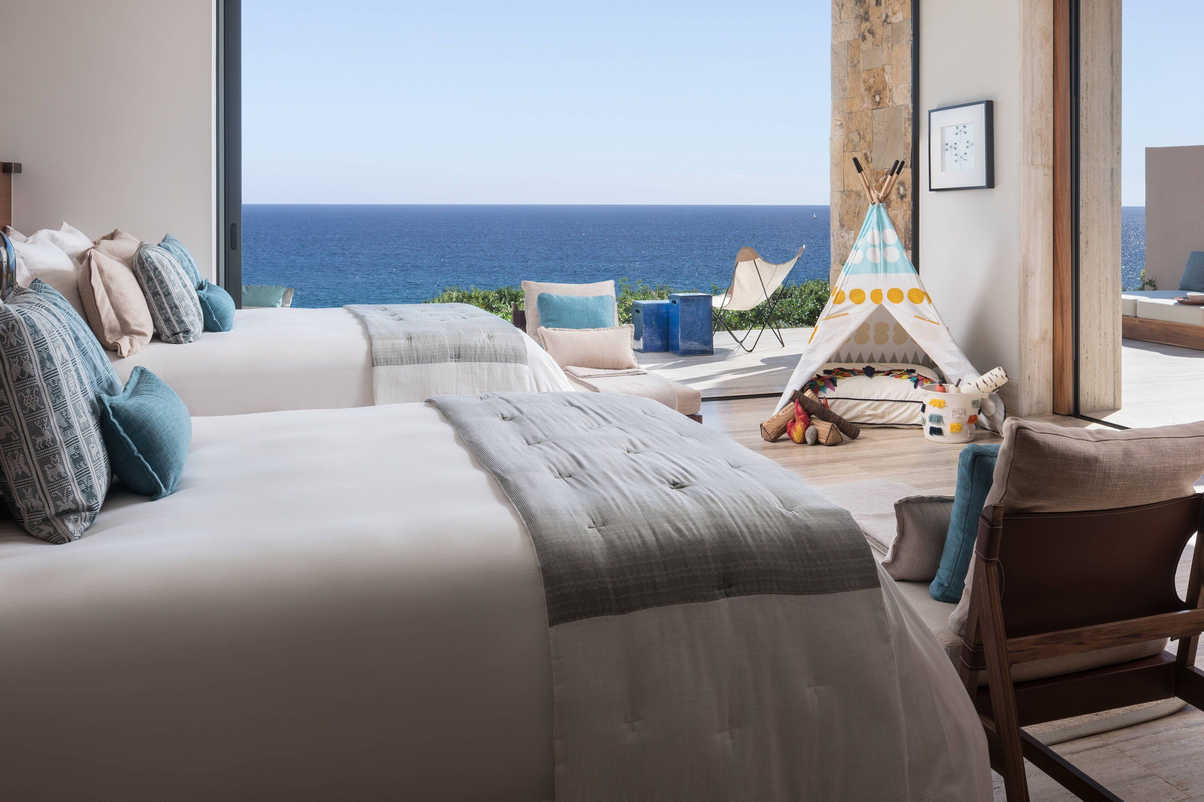 A bedroom with two beds, a view of the sea, a teepee, and a chair.