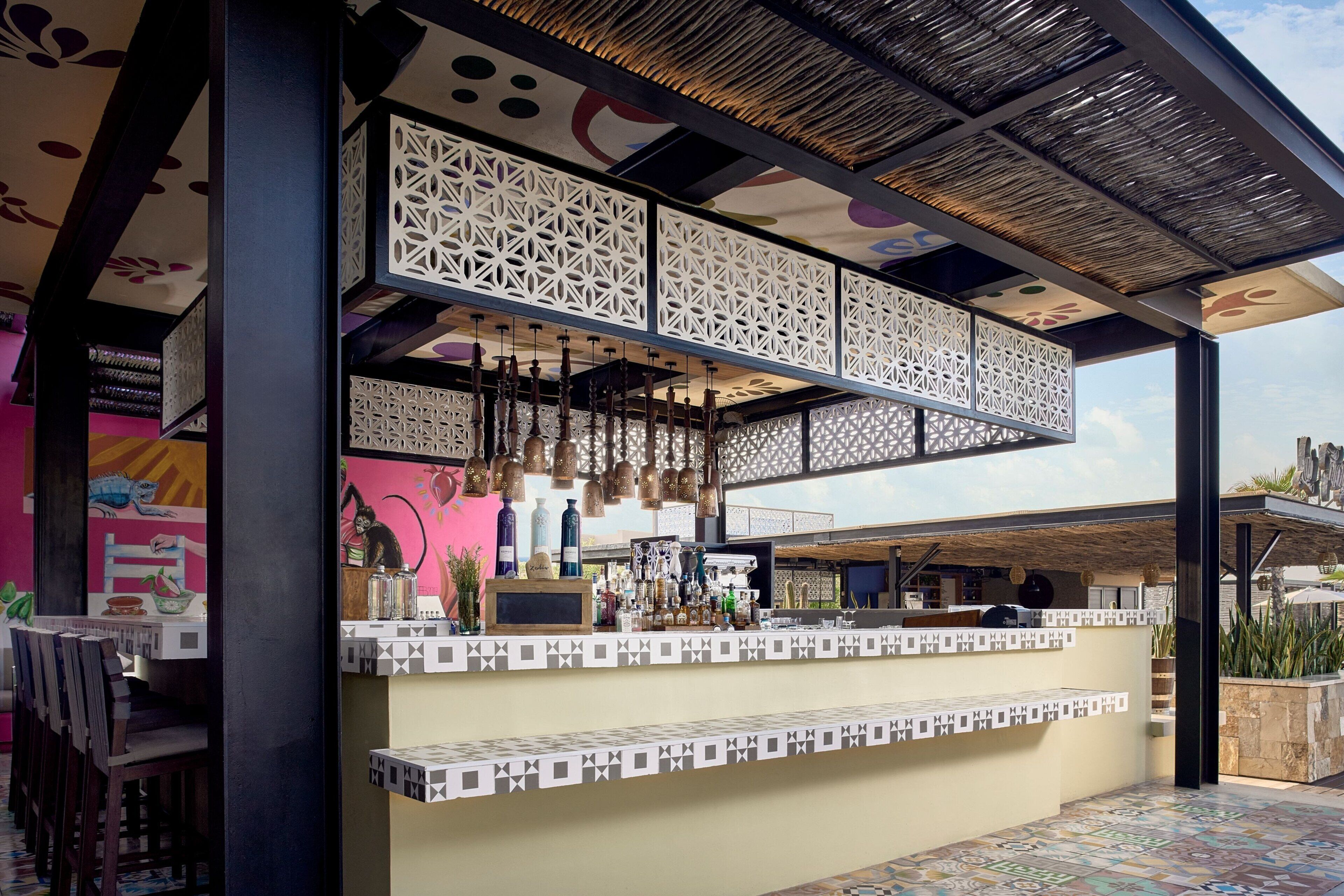 Zona de bar con techo estampado, luces colgantes y barra con botellas.