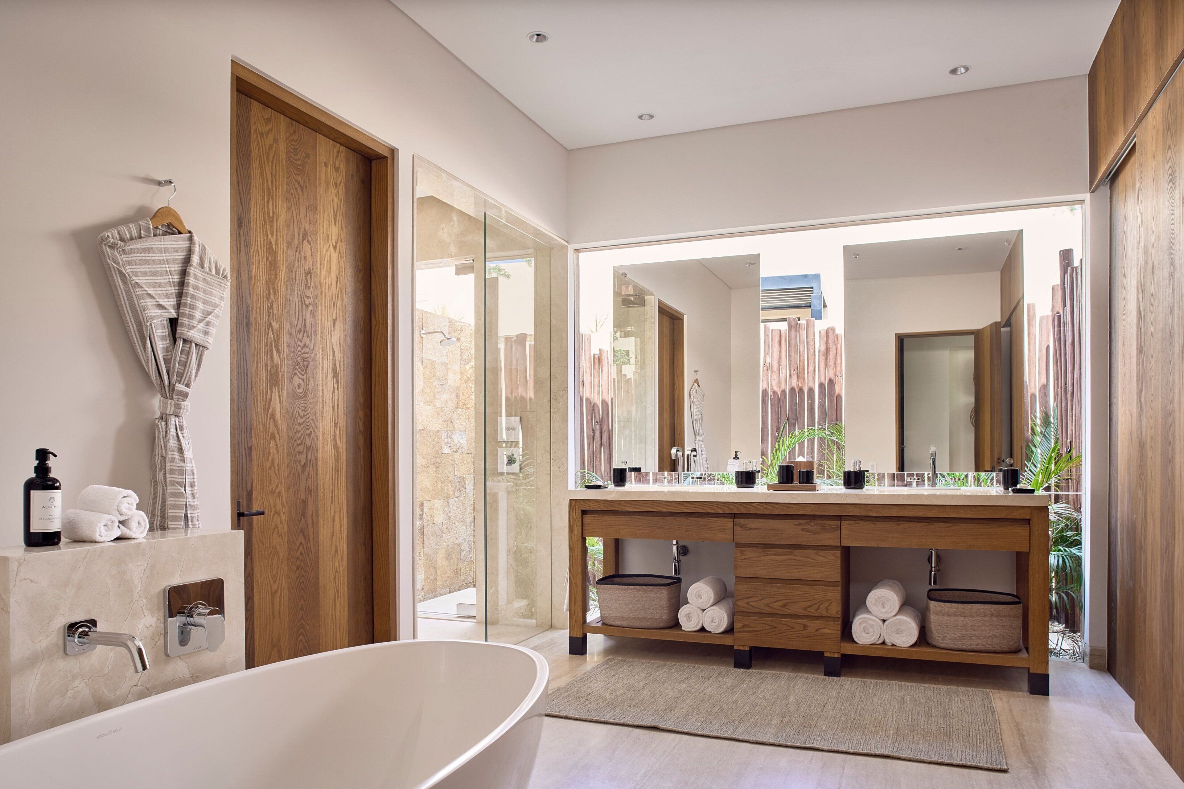 Un baño moderno con una bañera independiente, tocador de madera y un espejo grande.