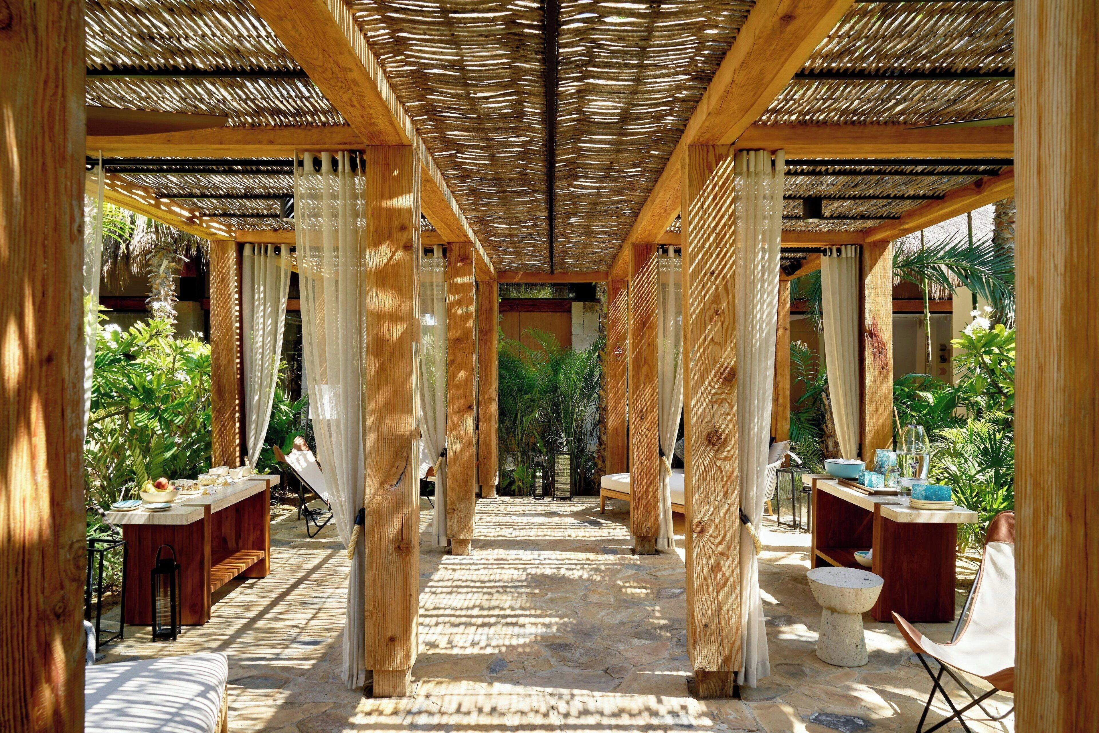 A covered outdoor area with wooden pillars, stone flooring, and a central pathway leading to a seating area.