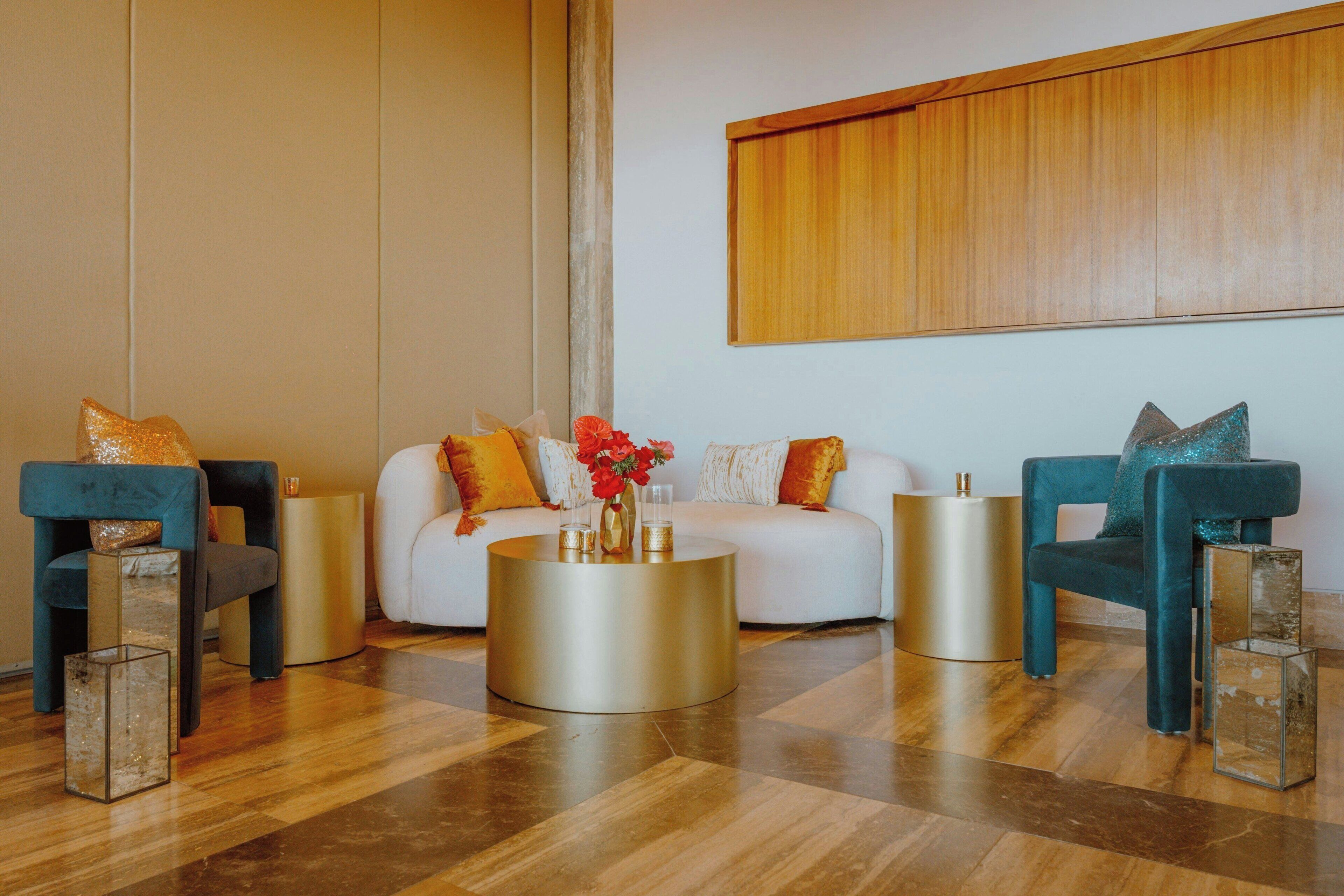 Un salón moderno con un sofá blanco, dos sillones color turquesa y una mesa de centro redonda dorada.