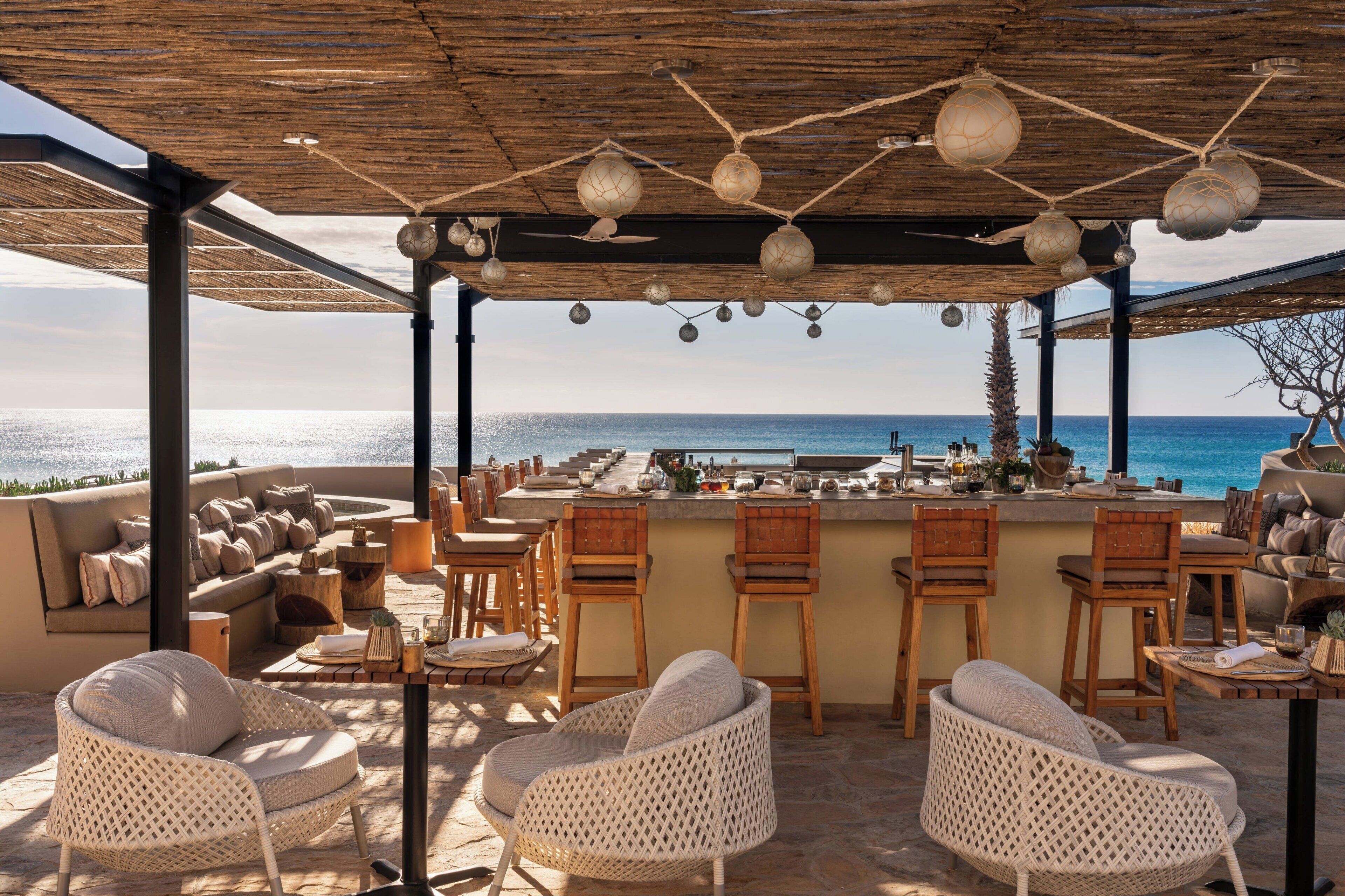 An outdoor bar area with wicker furniture, a wooden ceiling, and a view of the sea.