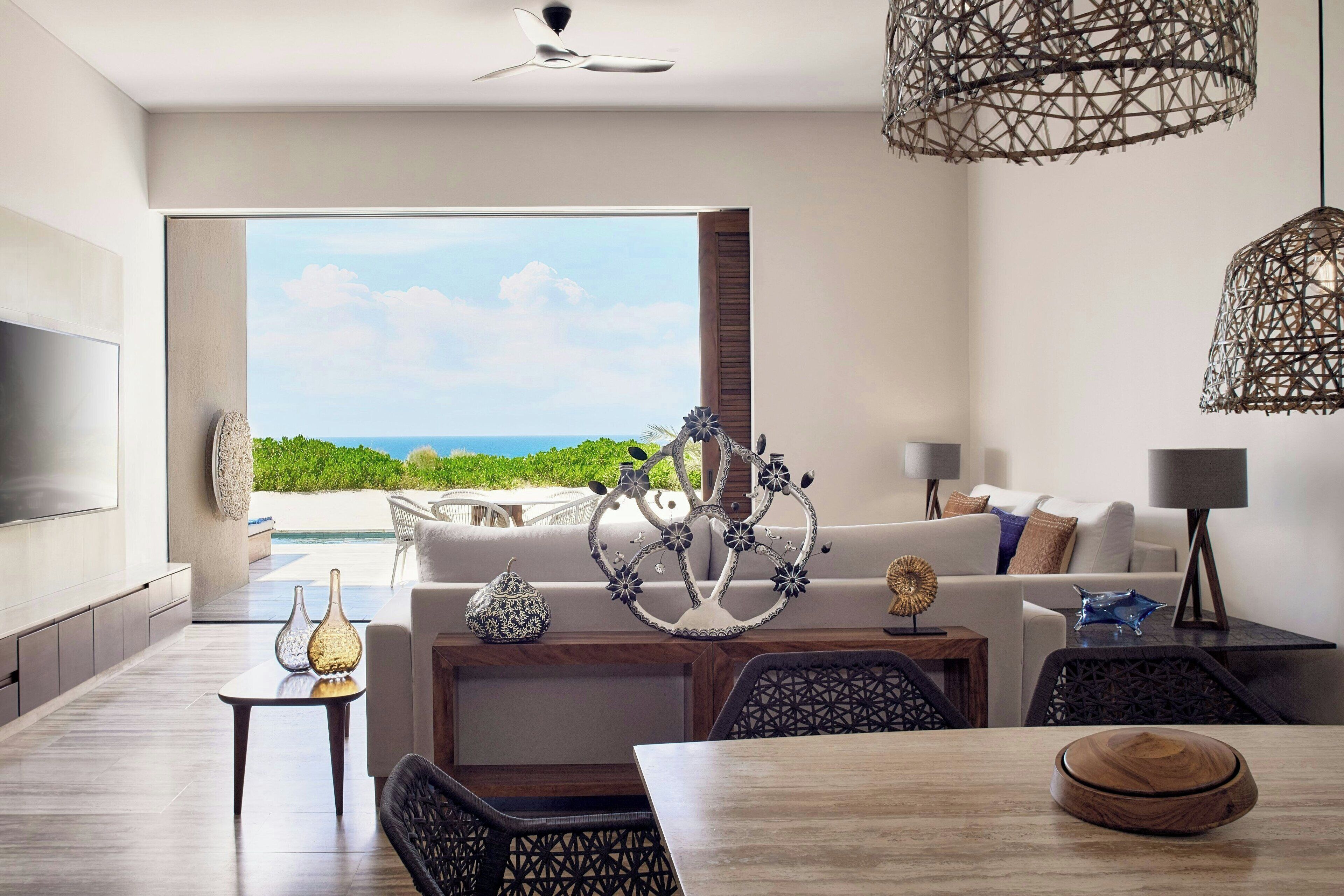 A modern living room with a large TV, a dining table, and a view of the ocean.