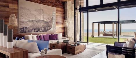 A modern living room with a large painting, wooden furniture, and a view of the beach.