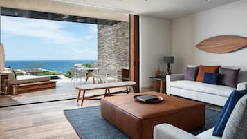 A modern living room with a view of the ocean, a sofa, a coffee table, and a dining area.