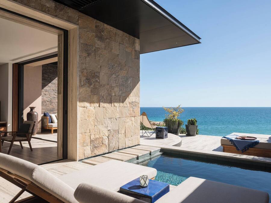 Uma área de piscina moderna ao ar livre, com vista para o mar, paredes de pedra e espreguiçadeiras.