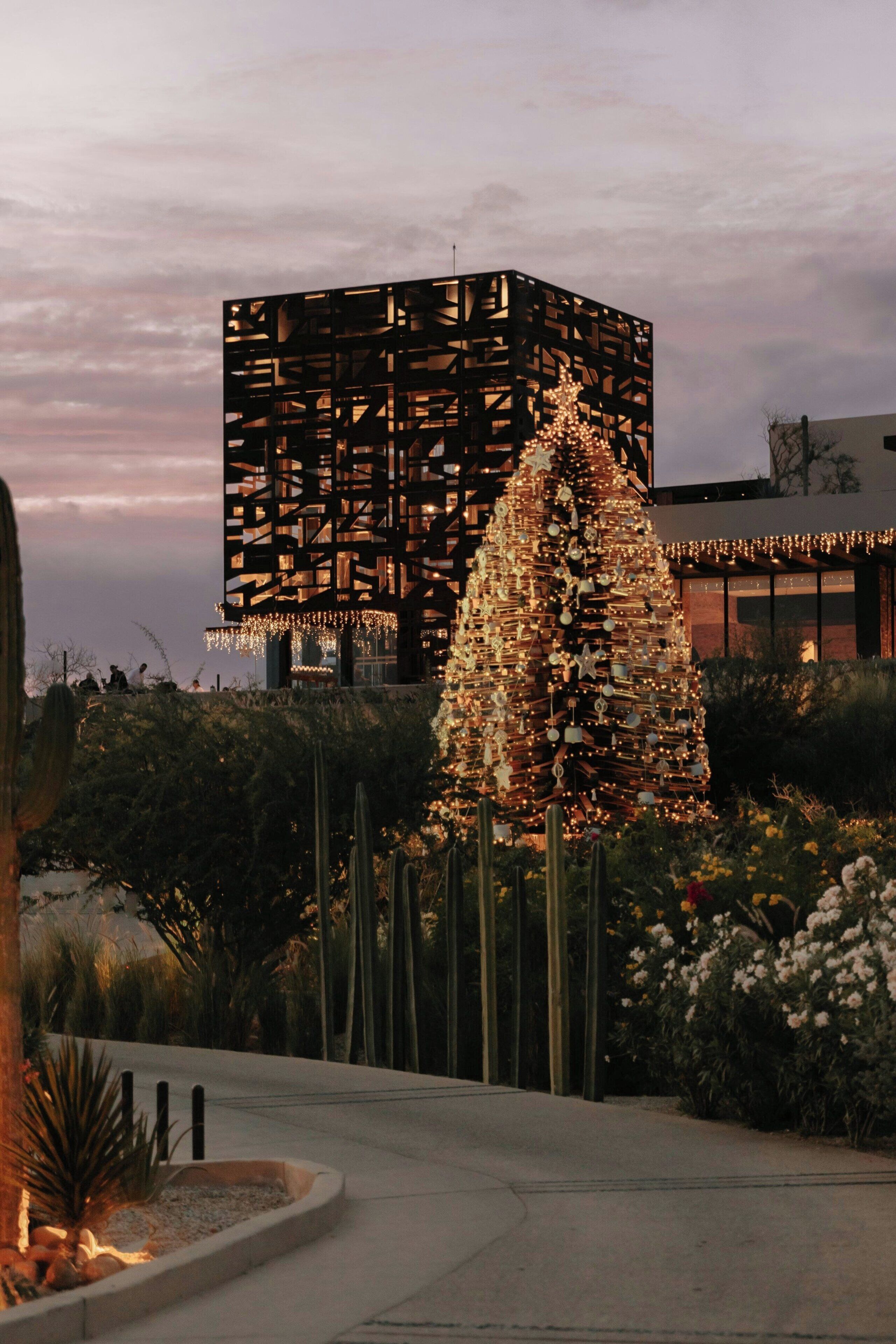 Ein modernes Gebäude mit einer markanten, geometrischen Fassade und ein großer, beleuchteter Weihnachtsbaum im Vordergrund.