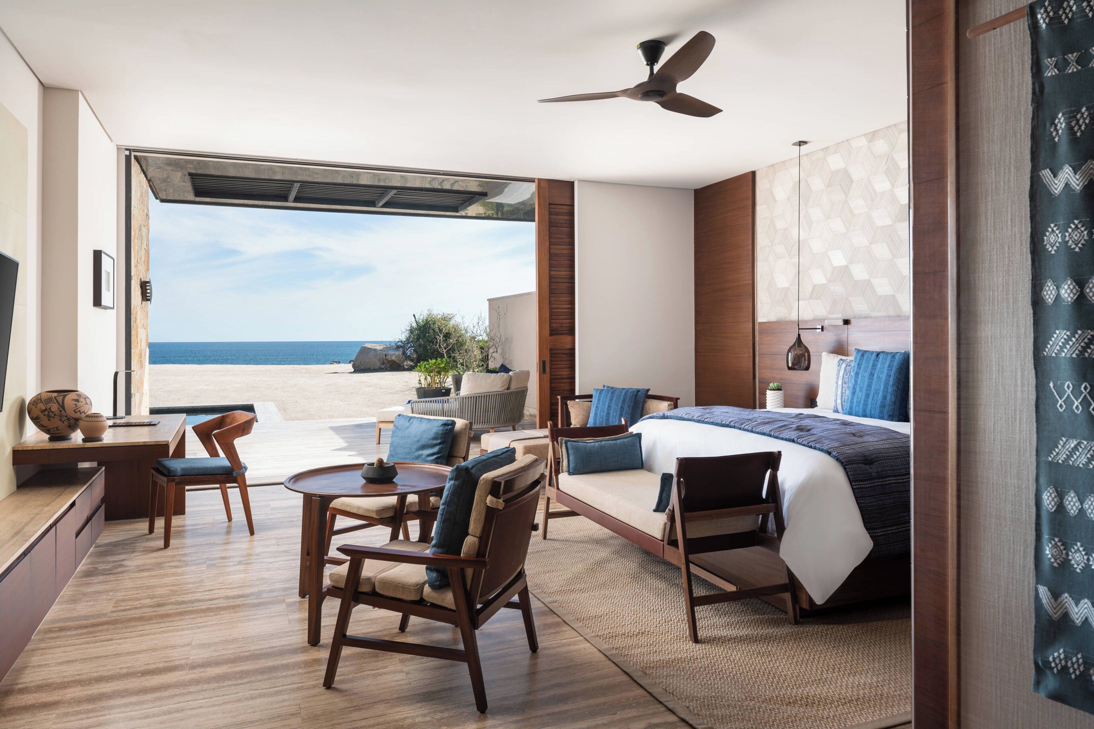 A modern hotel room with a large bed, a desk, and a seating area with a view of the beach.