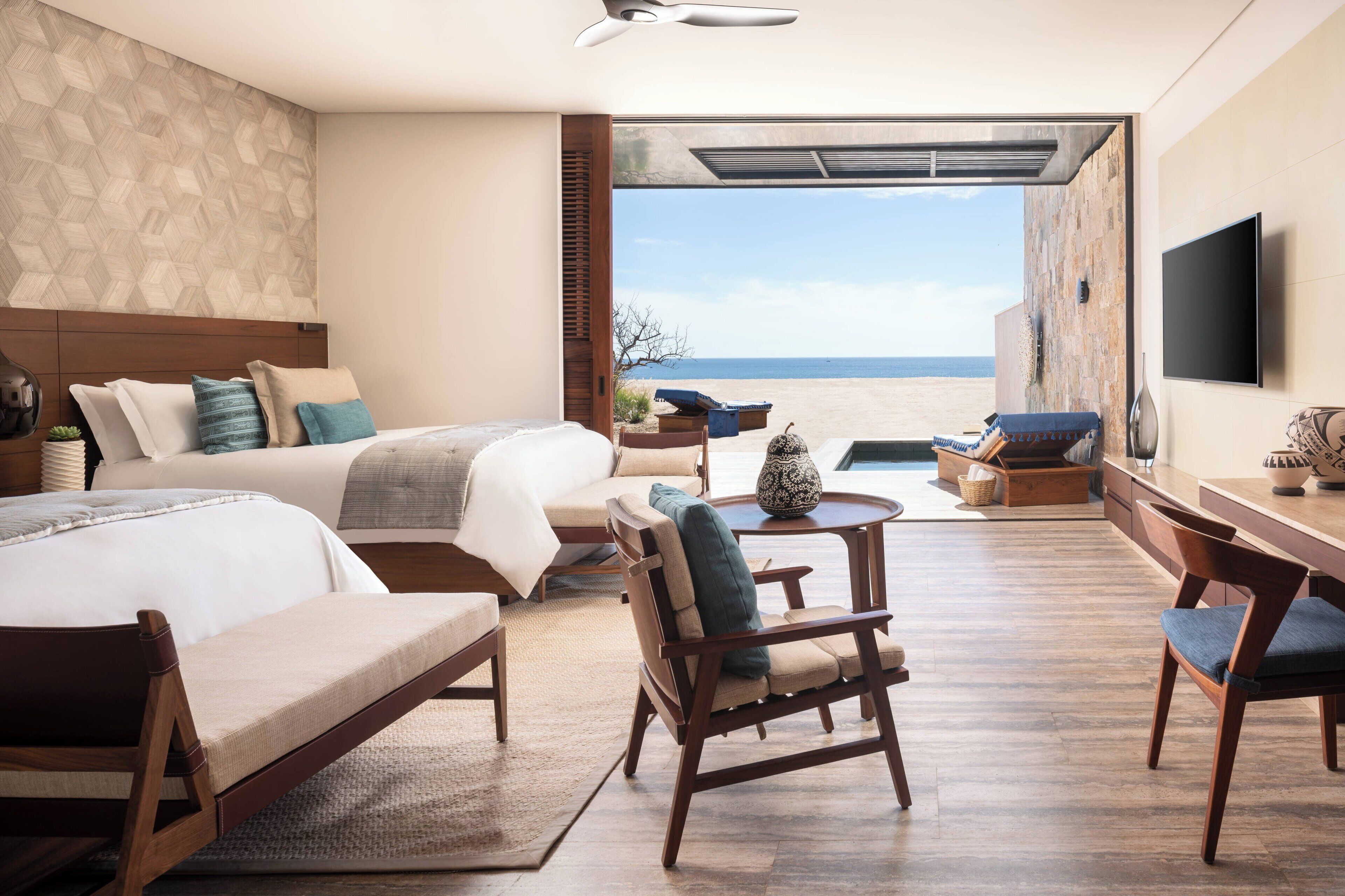 Une chambre d’hôtel avec un lit, un bureau, une chaise, une petite table et une vue sur la plage.