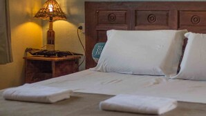 Una cama bien hecha con sábanas y almohadas blancas, una mesita de noche de madera con una lámpara y un cabecero de madera.