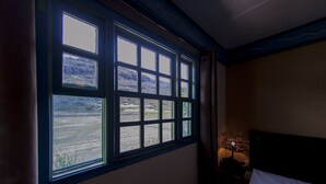 Una habitación con un ventanal grande, una cama y una mesita de noche con lámpara.