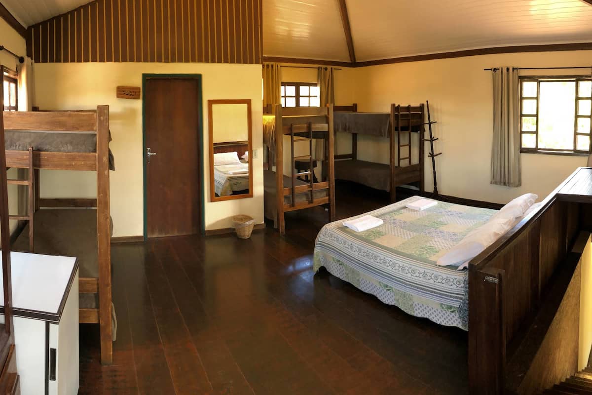 A room with bunk beds, a desk, a mirror, a television, and a window with curtains.