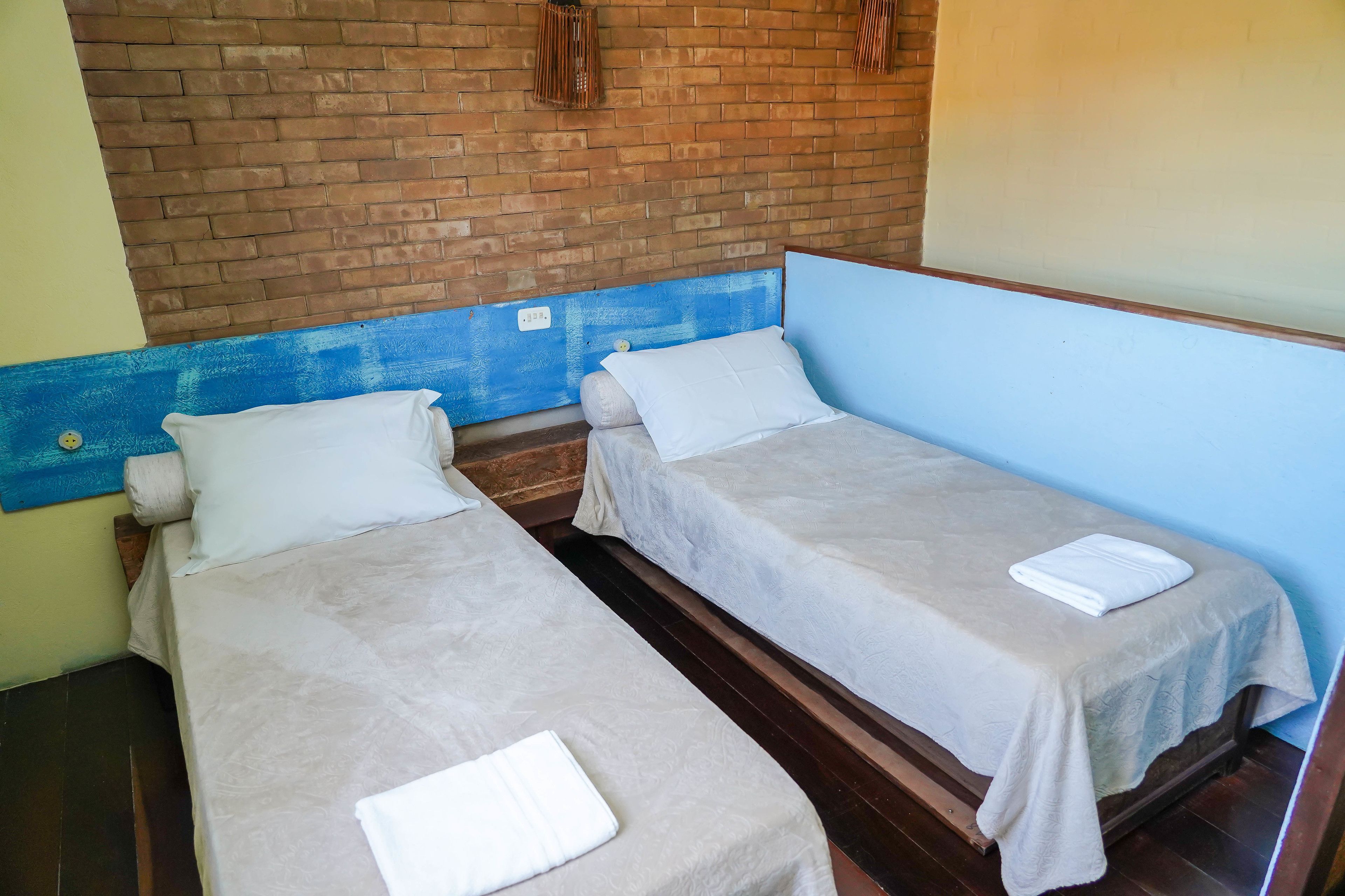 Two single beds with white linens, a brick wall, and a blue painted section.
