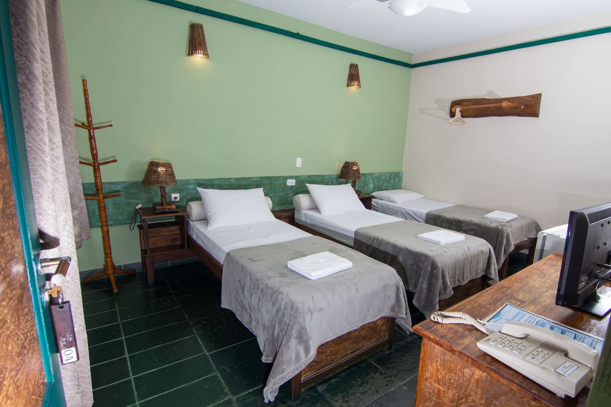 A hotel room with three single beds, a desk with a telephone, and a computer.