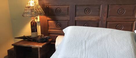 A bed with a white quilt, a wooden nightstand with a lamp, and a wooden headboard.